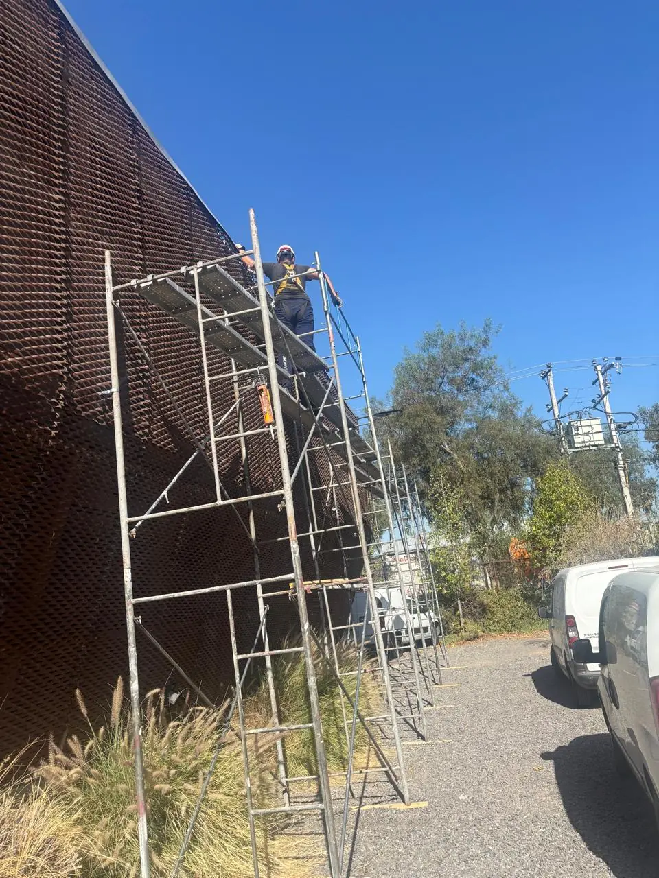 Operario con casco y arnés en nivel superior de andamio - Servicios Urgentes